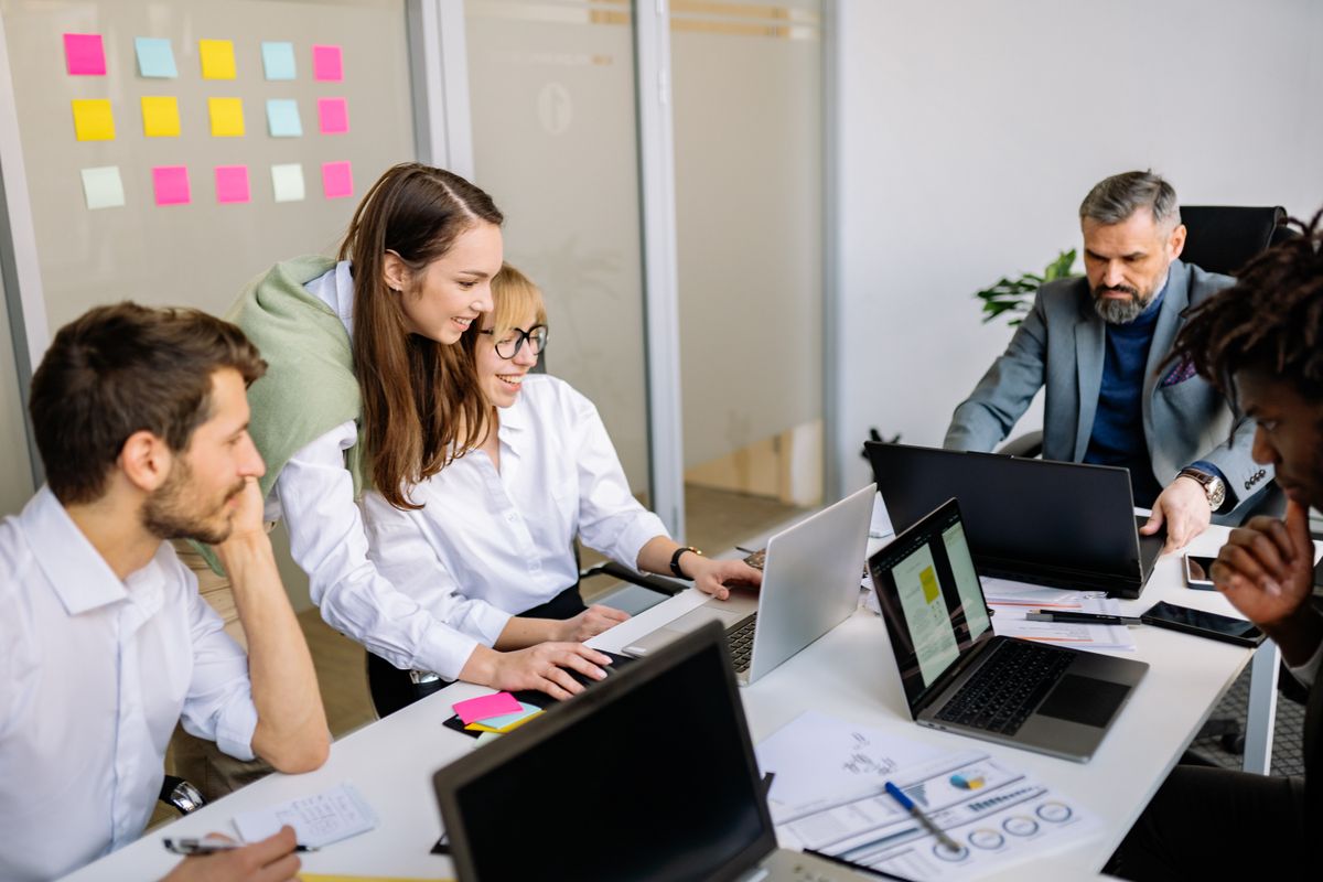 A small team of colleagues collaborates around laptops and documents in an office, representing AI automation layered onto an existing team rather than replacing it