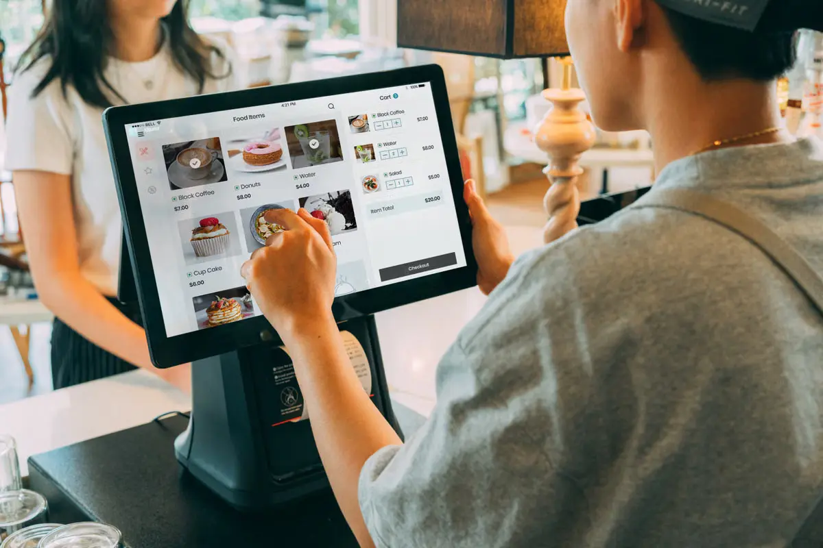 A retail employee assists a customer at a checkout counter using a point-of-sale system