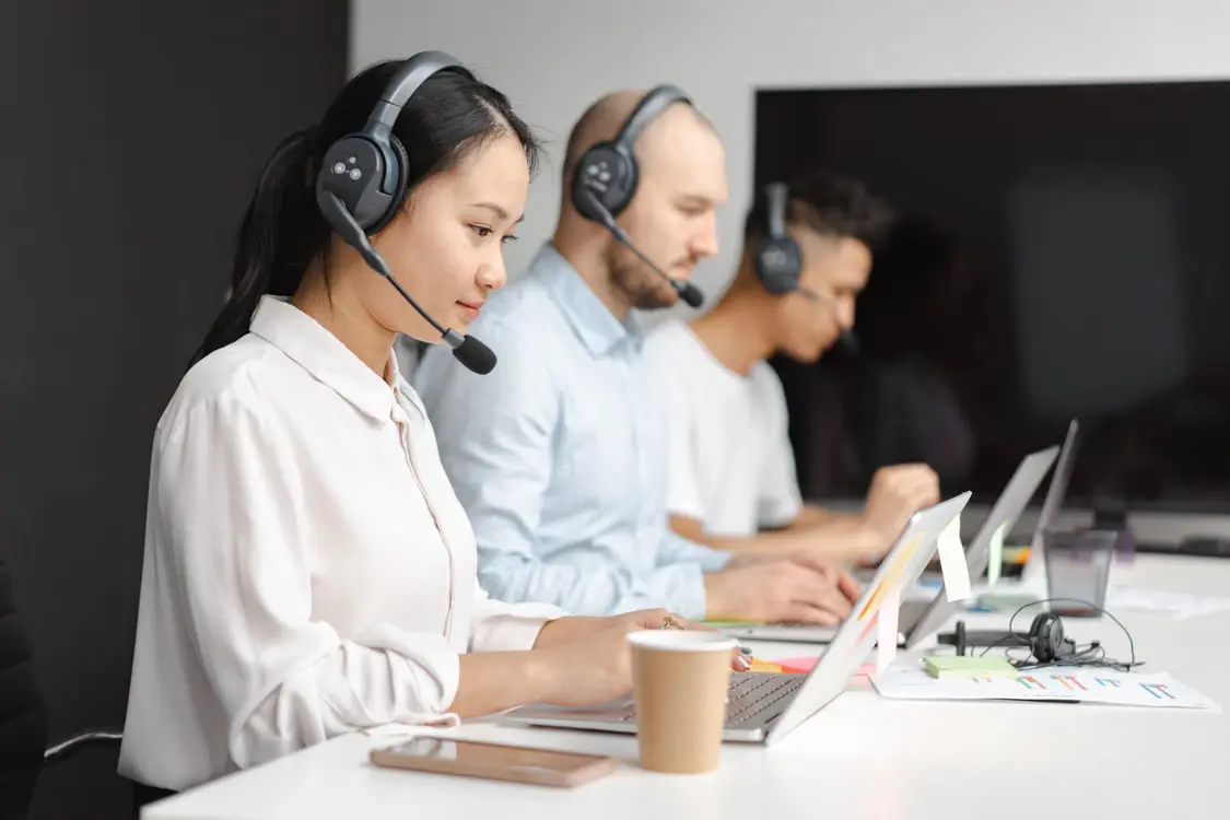 A customer service professional focuses on her laptop screen while managing calls in a modern office