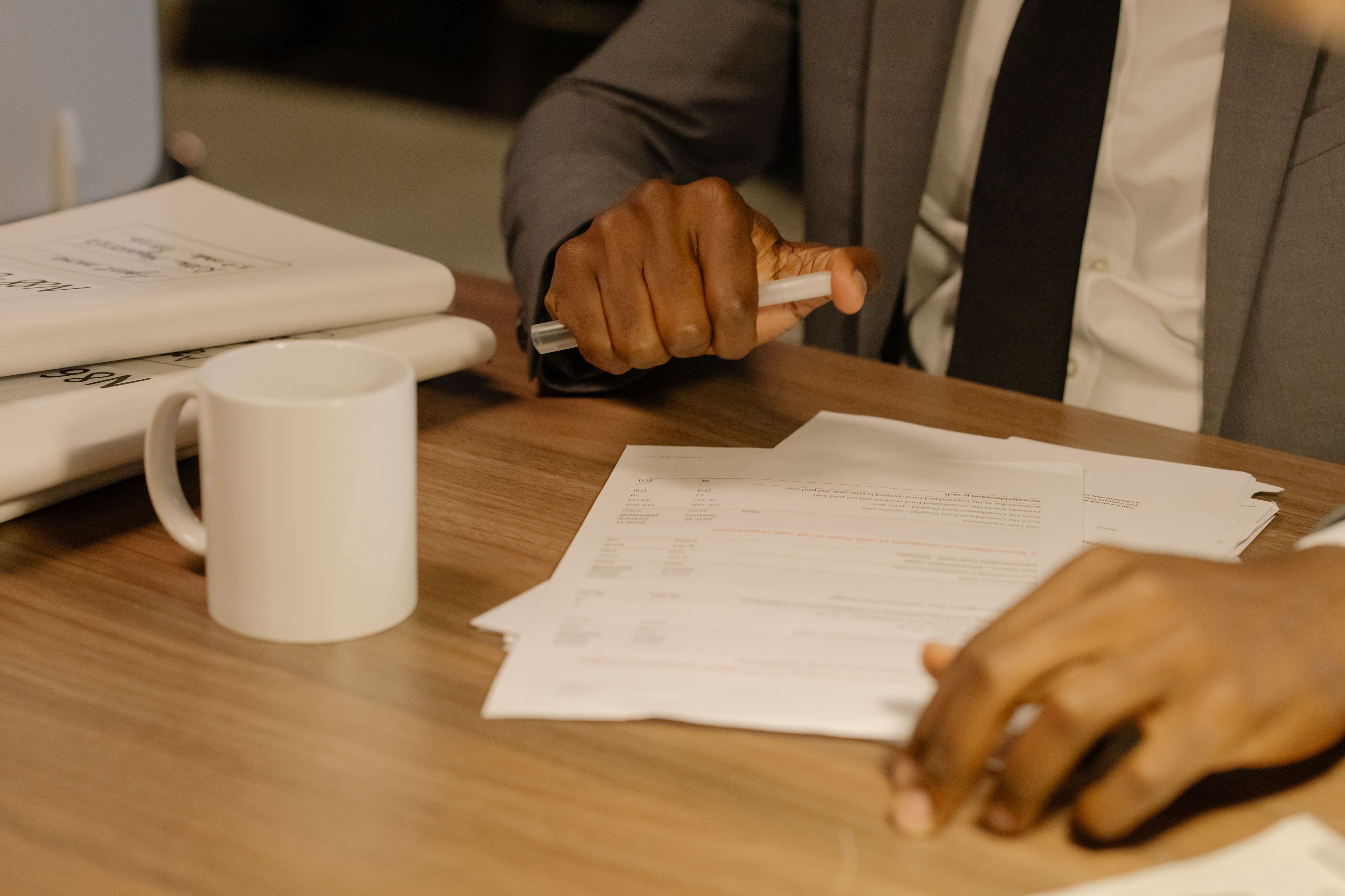 A professional in a suit reviews paperwork and reports at a wooden desk