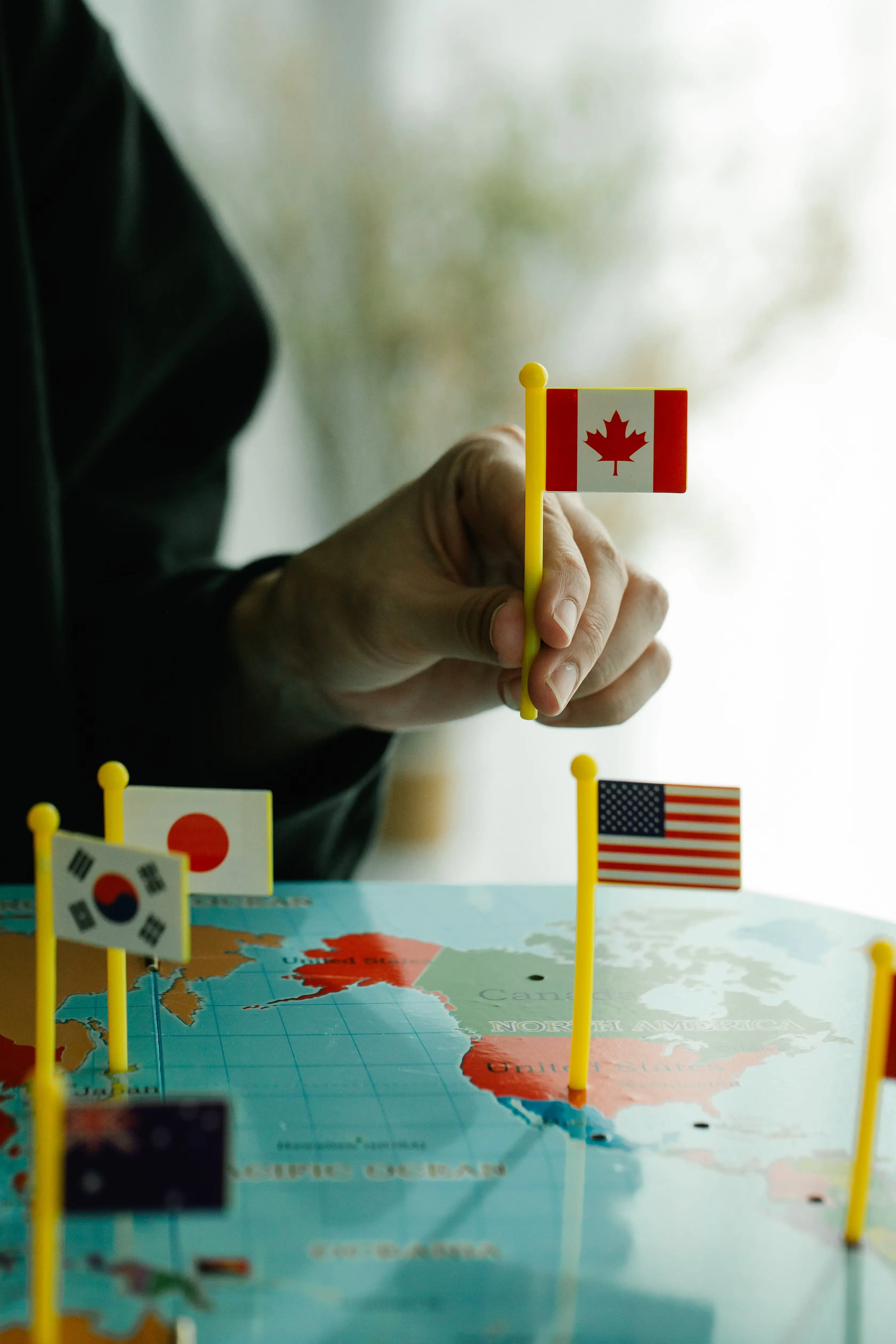 A hand placing national flag markers on a world map, illustrating country-by-country study permit allocation limits