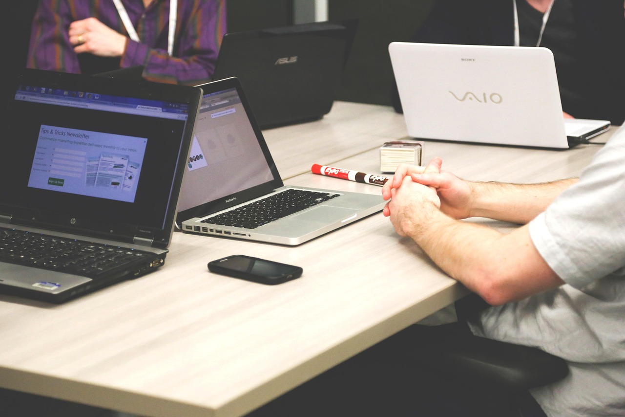 A small team gathered around a table with several different laptops open, reviewing a shared budget