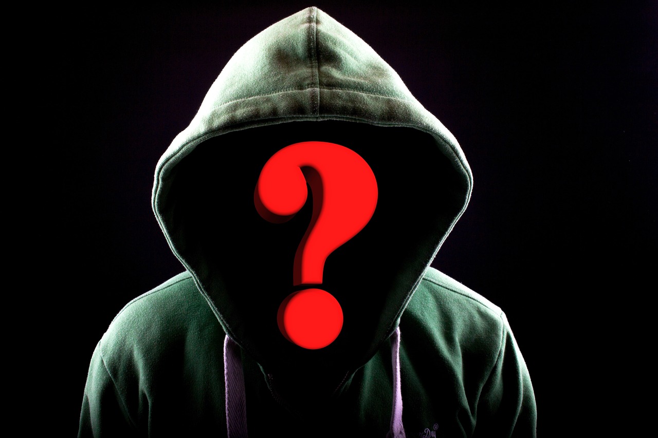 Hooded figure at a laptop with a glowing question mark, symbolizing the anonymity of AI-powered fraud attacks on Canadian businesses in 2026