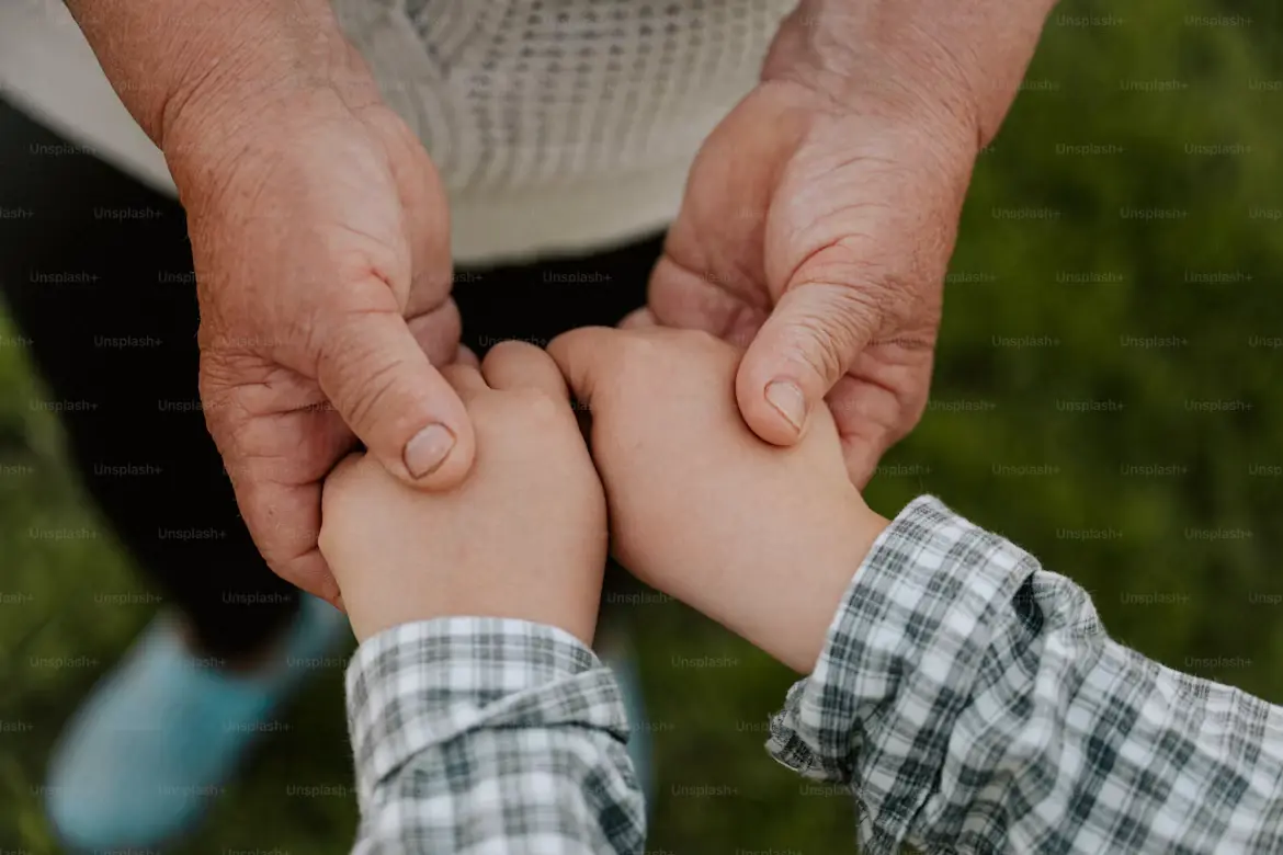 An elder gently holding a young child's hands, representing the emotional core beneath a legacy plan