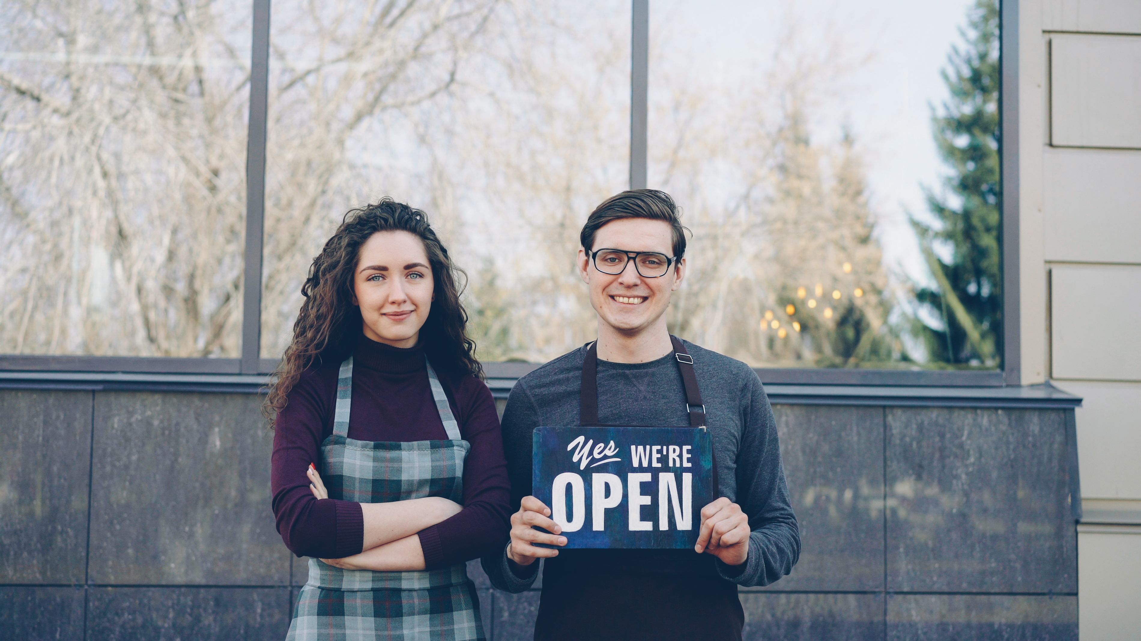 Two small business owners stand together holding a Yes We're Open sign, representing resilience amid Canada's 2026 small business confidence data