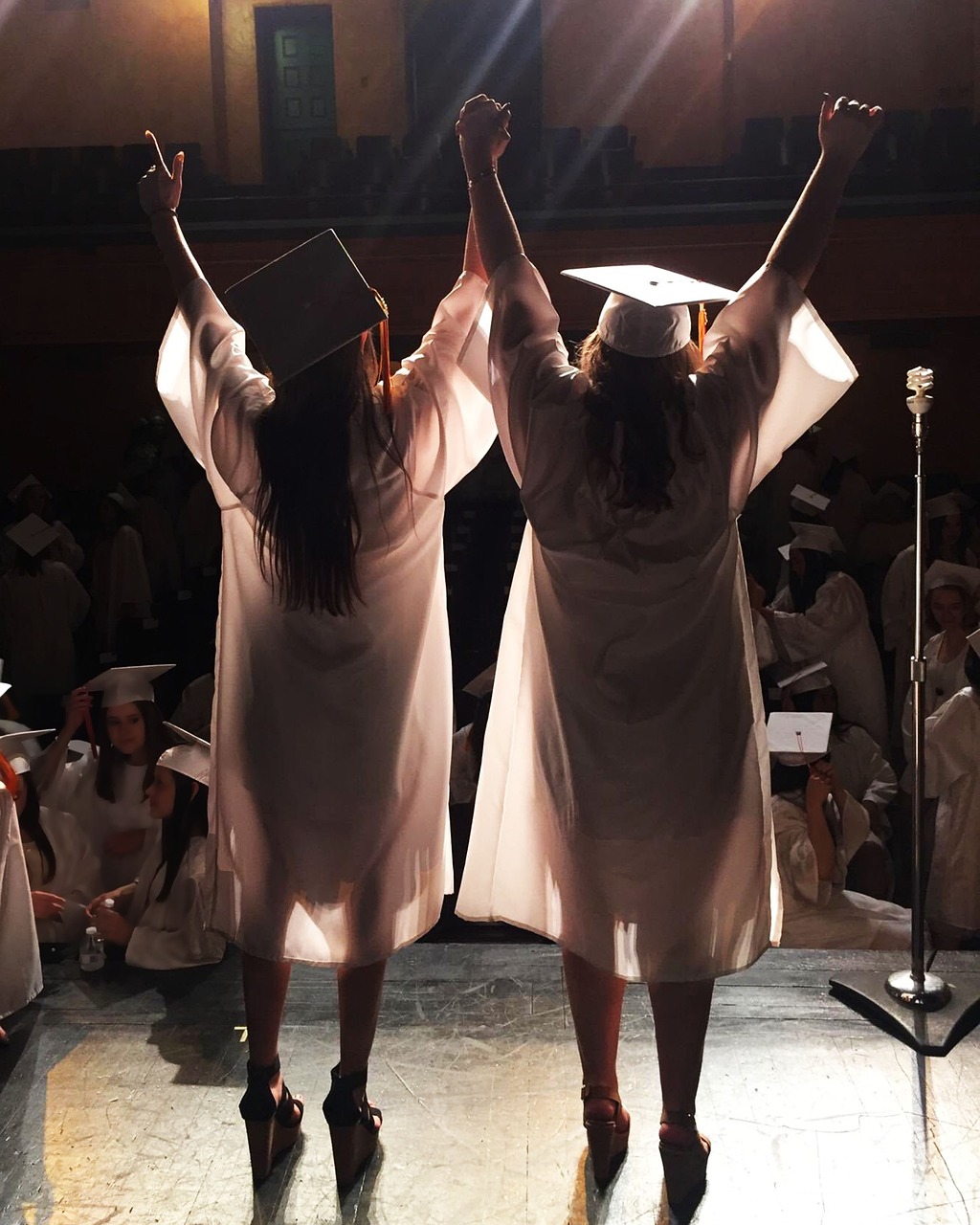 Two graduates in caps and gowns raising their arms on stage, representing the education outcomes CACD's programs are built to support