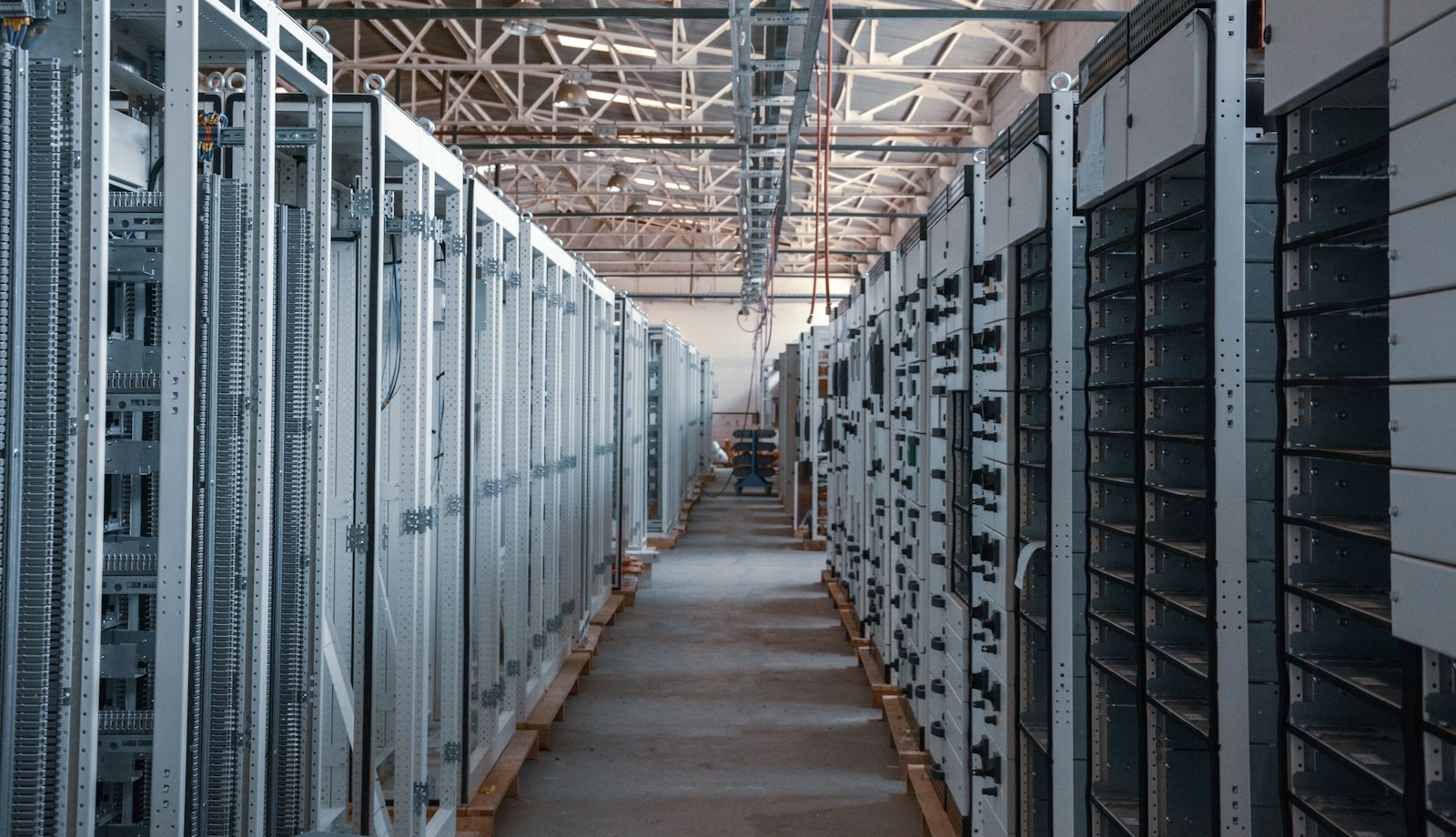 A long aisle between tall metal equipment cabinets in an industrial hall, representing the physical infrastructure behind computing and industry