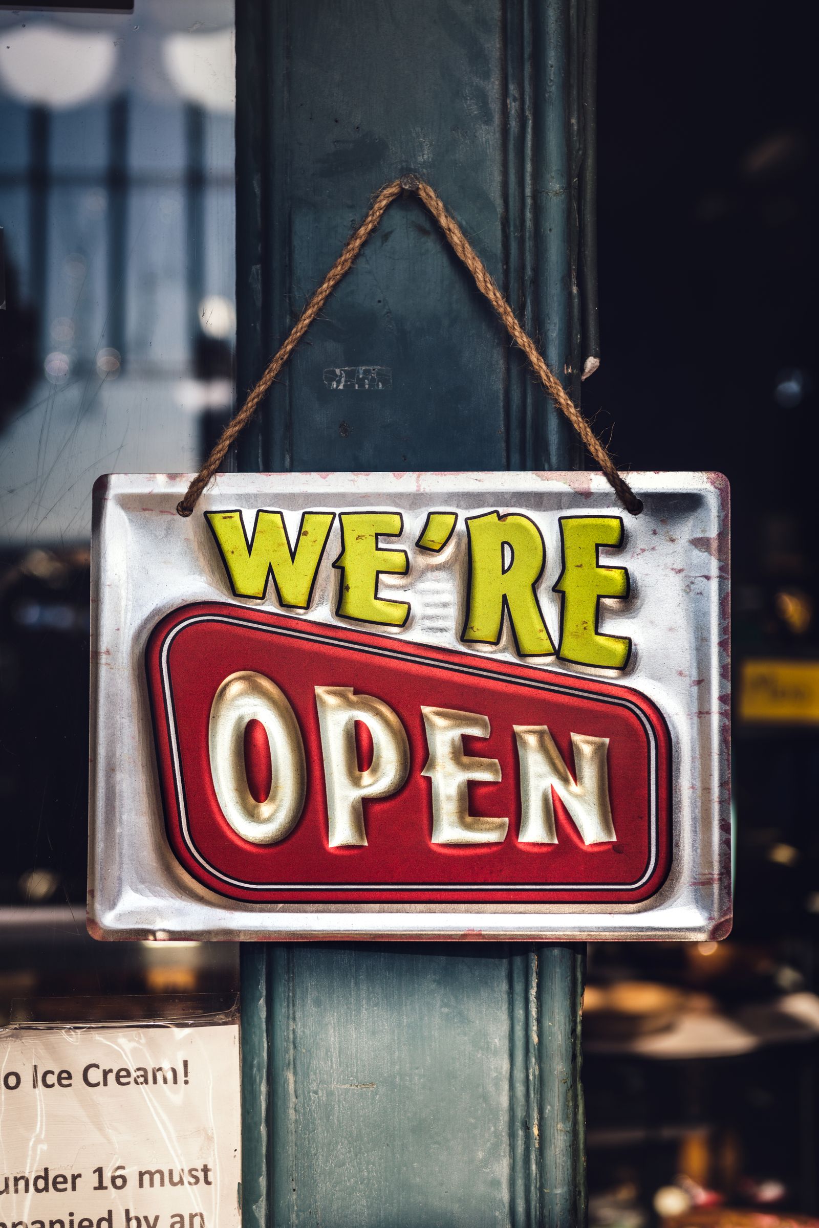 A vintage metal We're Open sign hanging on a shop door, symbolizing welcoming past customers back