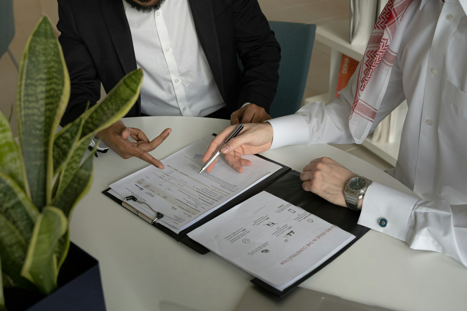 Two professionals at a table reviewing papers and writing with a pen, representing a founder planning profit decisions with an advisor