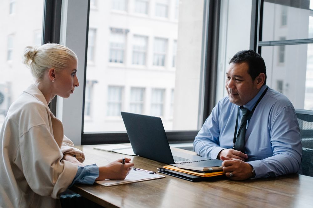 Employer asking questions of a female candidate filling in a job application form on a clipboard during a screening interview