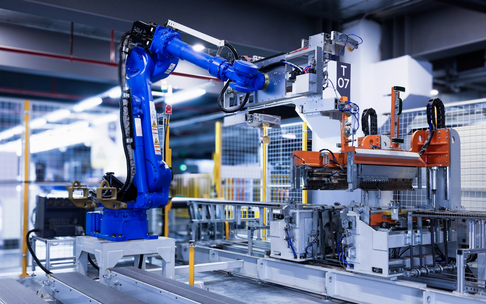 A blue industrial robot arm beside automated assembly equipment on a factory floor