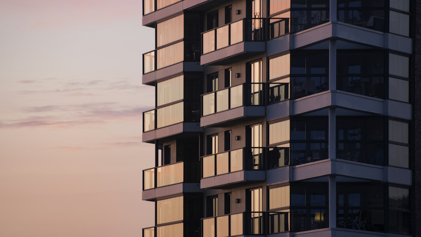 A modern apartment building with glass balconies glowing in warm evening light, representing residential property management
