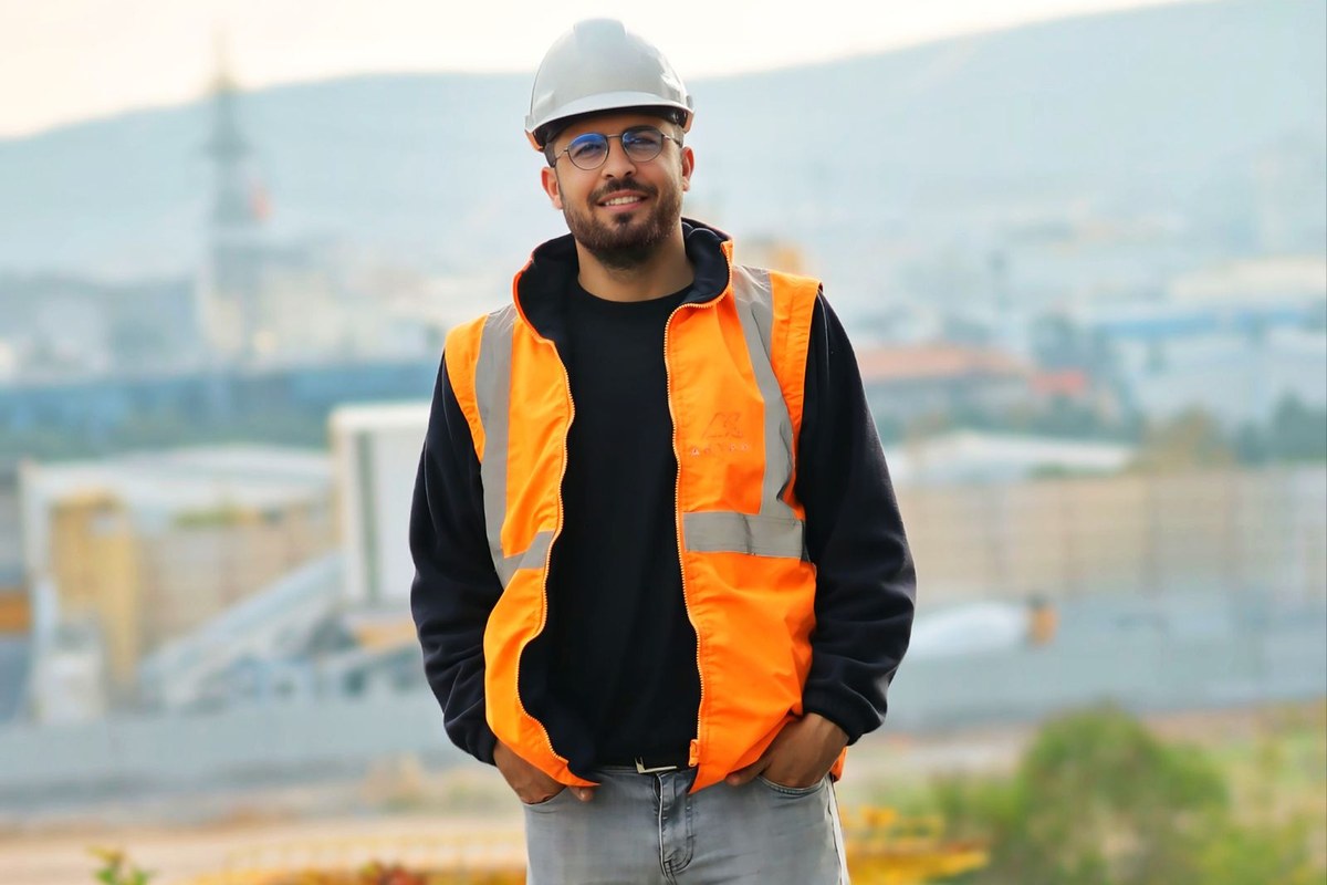 Smiling construction worker in an orange safety vest and white hard hat standing on a job site, representing Ontario tradespeople