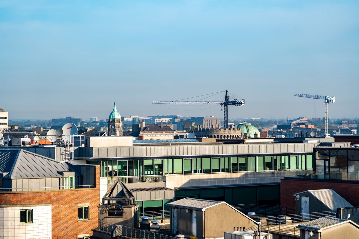 Tower cranes rising above a city skyline under a clear blue sky, representing construction activity in a major urban centre