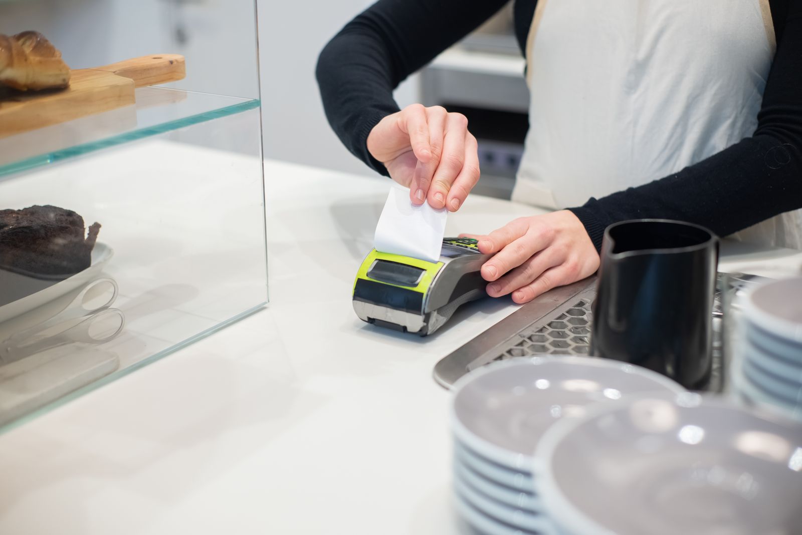 A cafe worker tearing a receipt from a card payment terminal on a counter