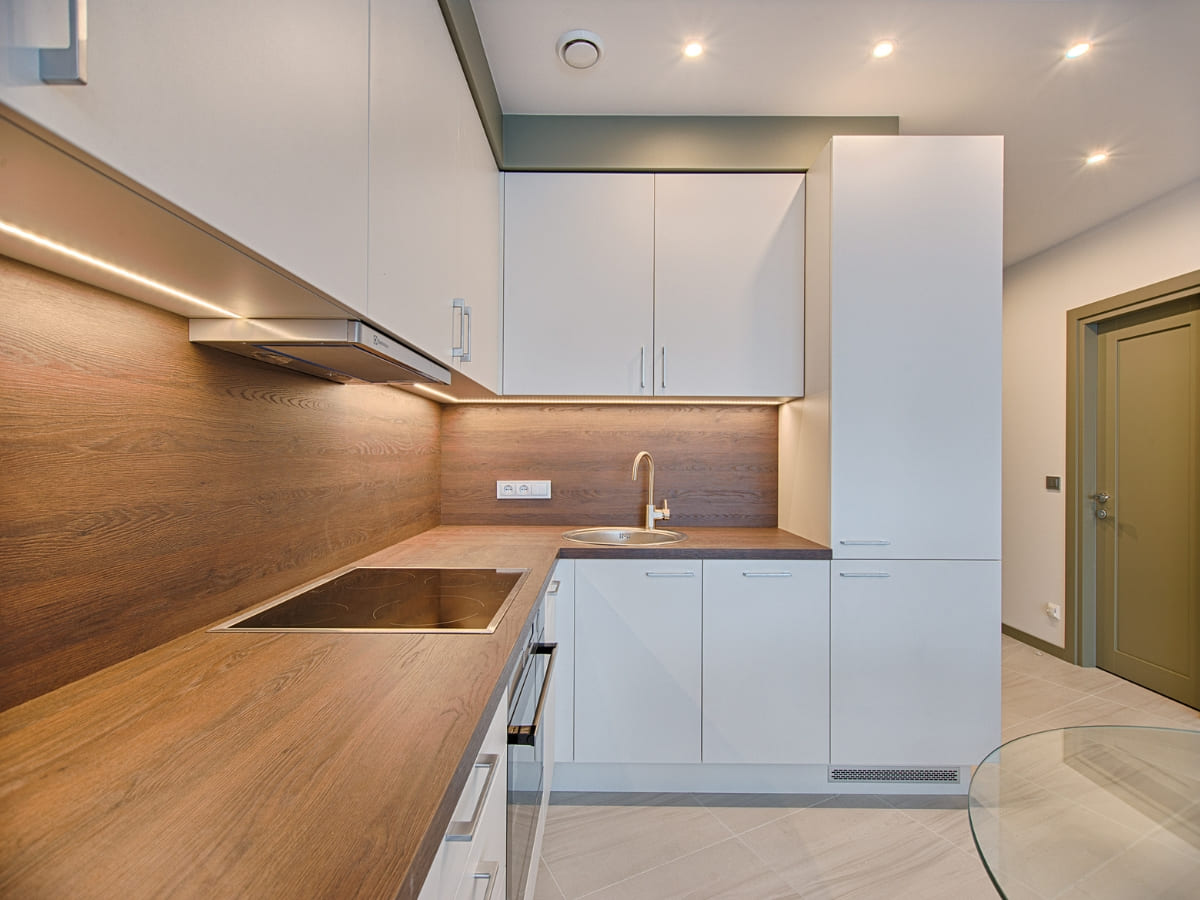 A small, modern kitchen with white cabinets, wood countertops, and under-cabinet lighting, creating a warm and functional space.