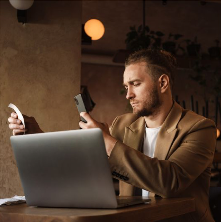 Un homme utilisant son téléphone pour scanner un ticket de caisse, avec un ordinateur portable devant lui, illustrant le processus de cashback en ligne.