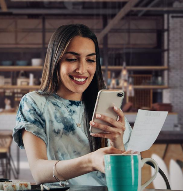 Une personne souriante utilisant son téléphone mobile et tenant un ticket de caisse, illustrant le processus de cashback.