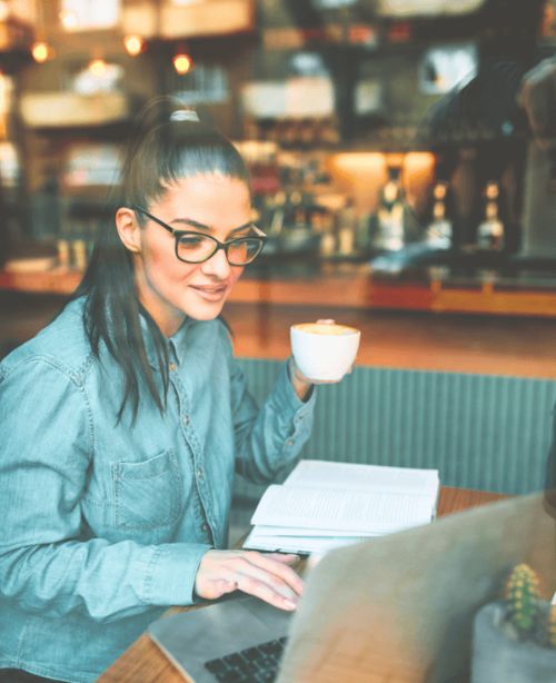 Image: Woman working on laptop in a coffee shop, symbolizing skills, tools, and support in end-of-life doula training.