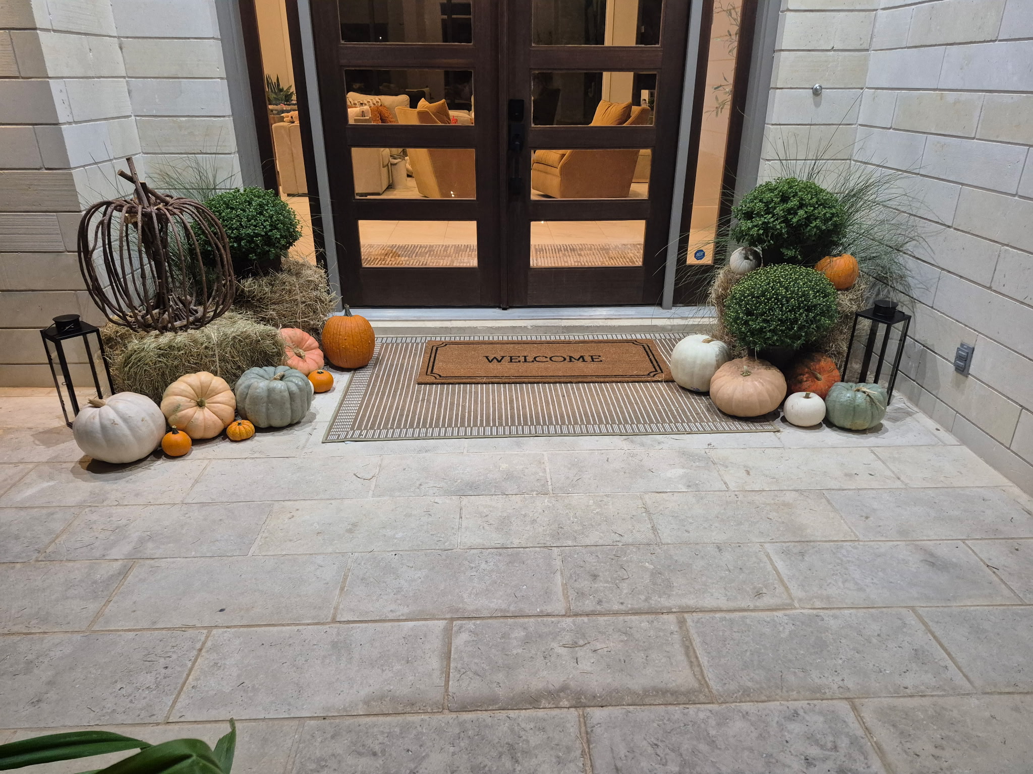 Double front doors framed by coordinated autumn displays of pumpkins, hay bales, mums, and lanterns