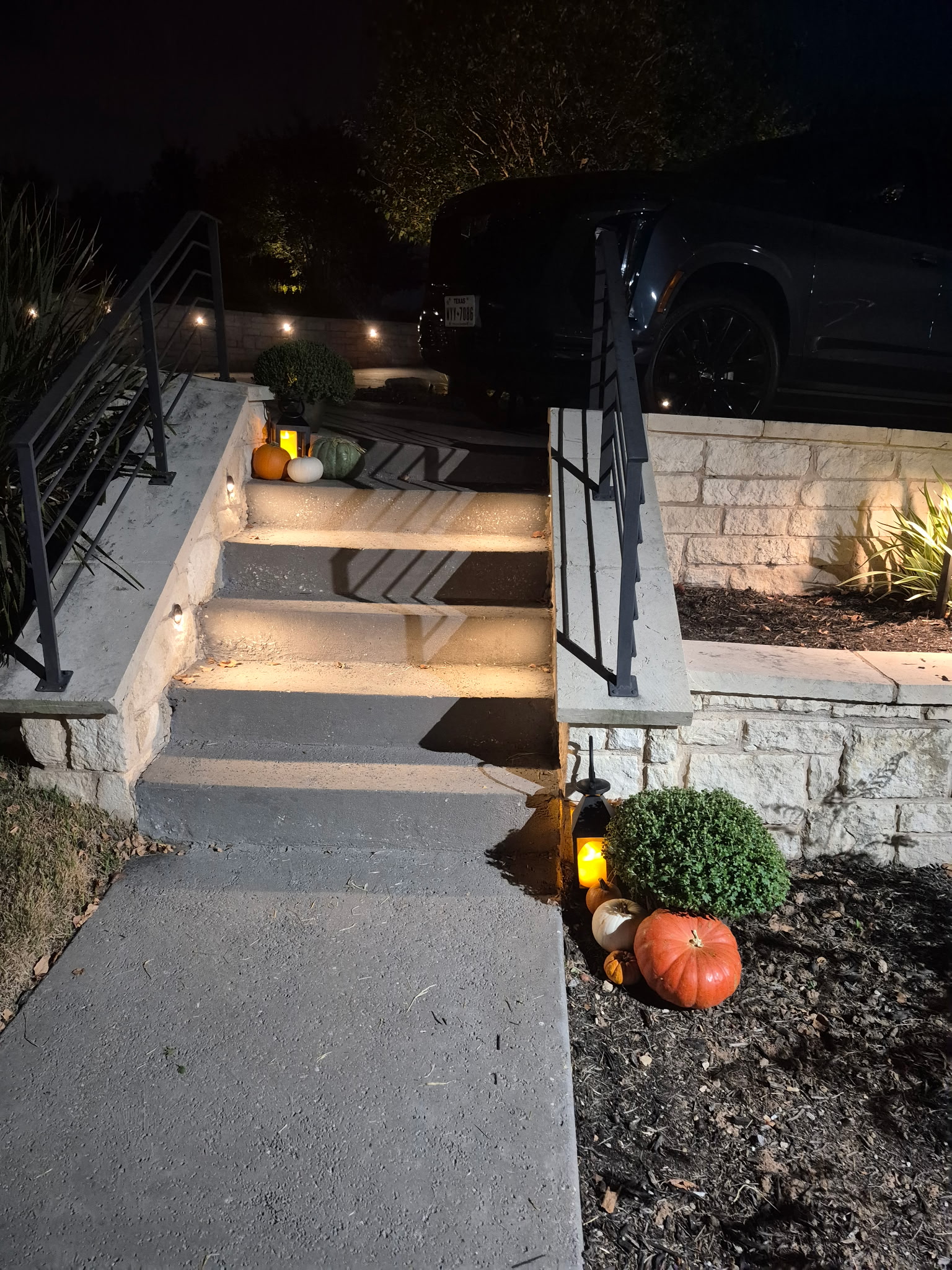 Outdoor stone steps decorated with pumpkins, mums, and glowing lanterns at night