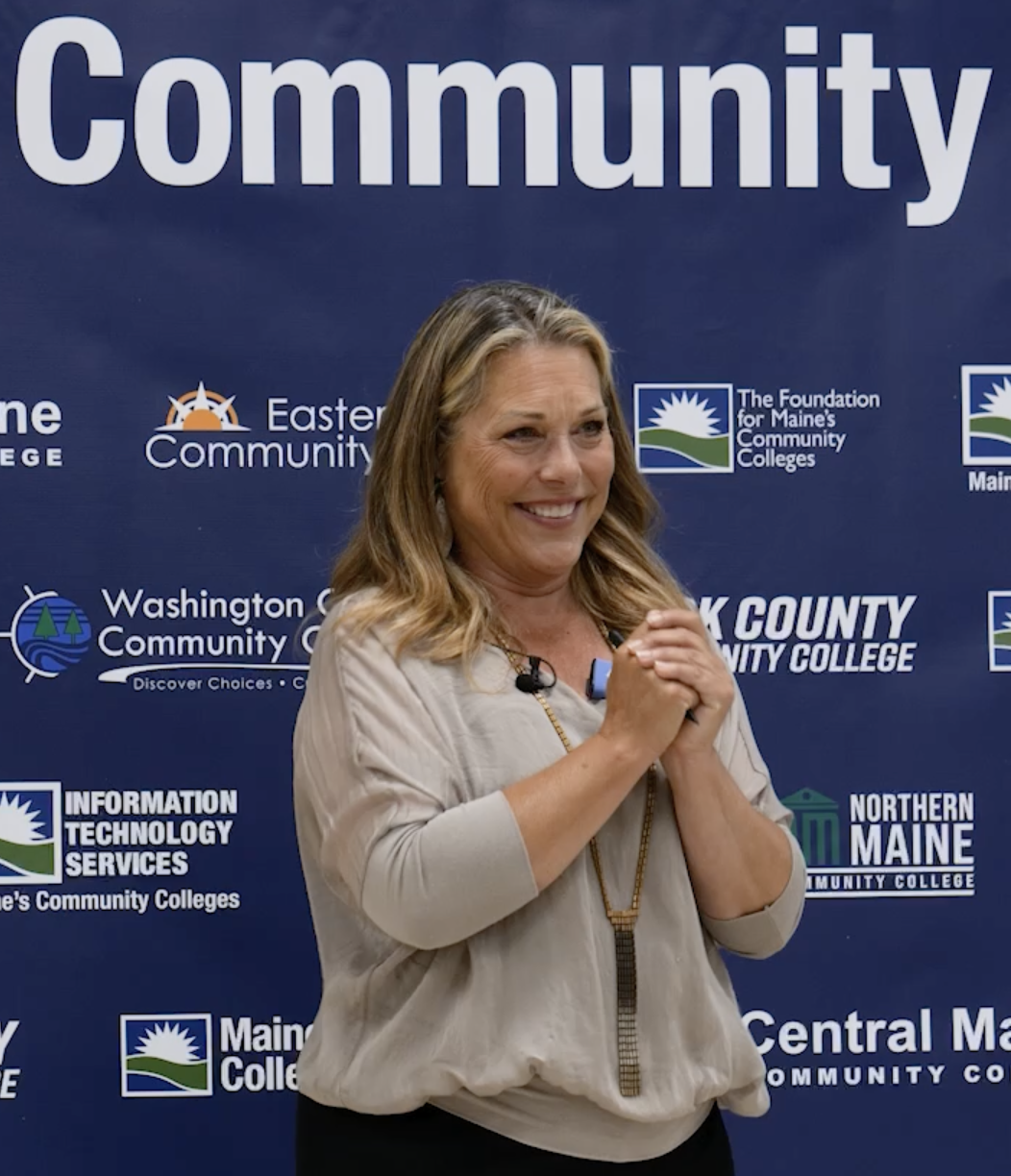 Pasha speaking on stage smiling, with hands clasped together at a Community event.