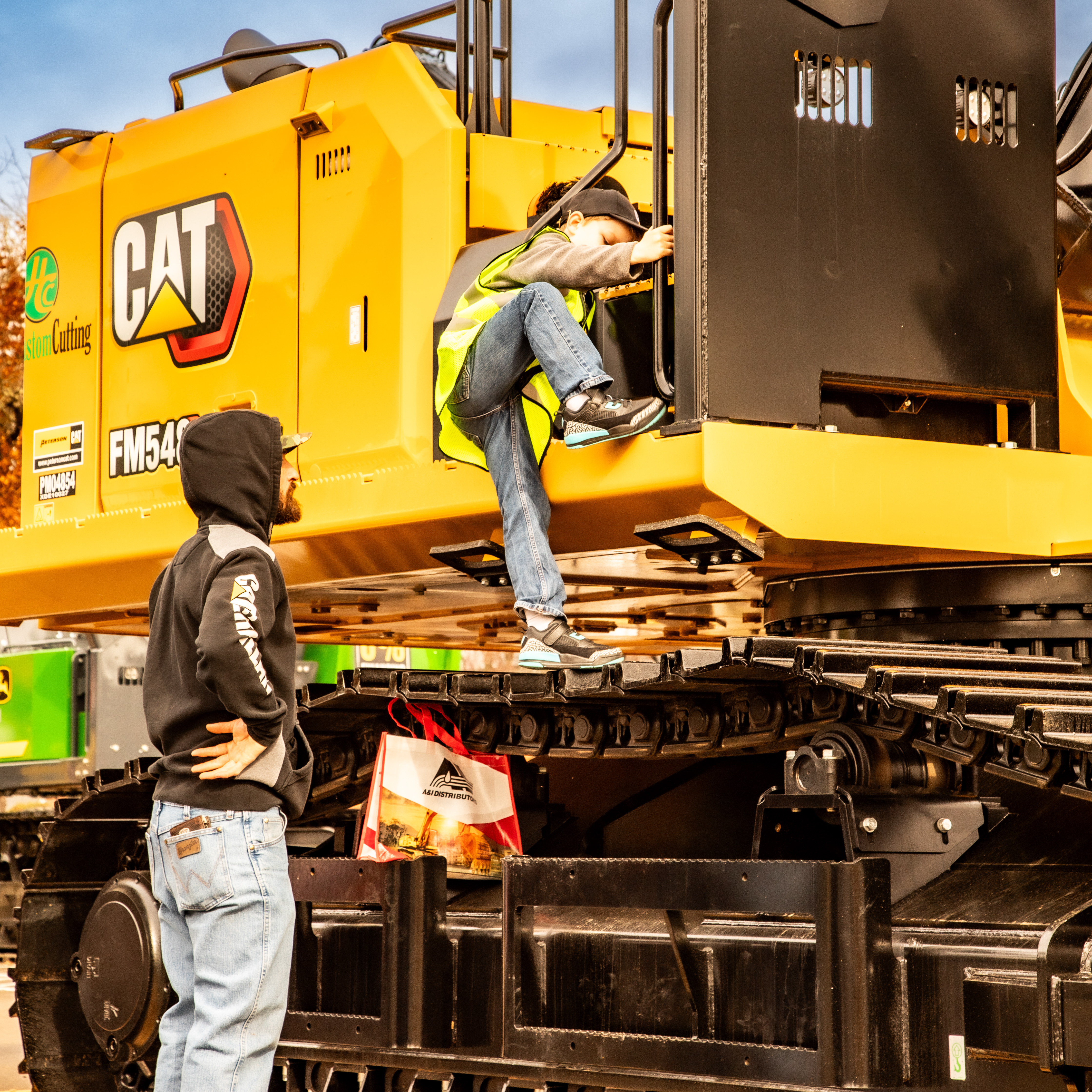 Professional commercial photography by Tyler Hills Photography: A child and father explore a new CAT FM54D excavator, highlighting the scale and design of heavy construction equipment in Salem, Oregon.