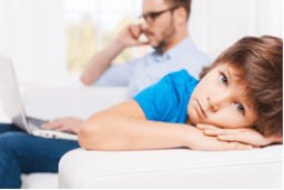 A young child looks sad while being ignored by busy parents, representing the formation of the belief 'I don’t matter unless I’m achieving something.' This visual illustrates how early emotional neglect creates subconscious patterns—known as Emotional Footprints—that impact emotional wellness and self-worth. A key focus of the Biko Method’s subconscious healing approach.