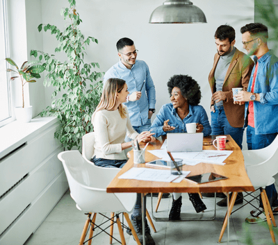A diverse team of smiling professionals reviewing a document together at a table, emphasizing the importance of emotional wellness and effective communication in the workplace.