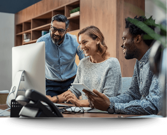 Three smiling colleagues gathered around a desktop in an office, representing the positive impact of the Biko® Method on corporate emotional wellness and team productivity.