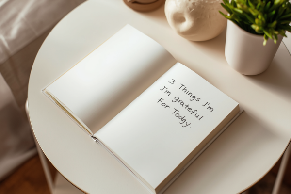 A bedside table or workspace with a gratitude journal open, showing a short list (e.g., “3 Things I’m Grateful For Today”).