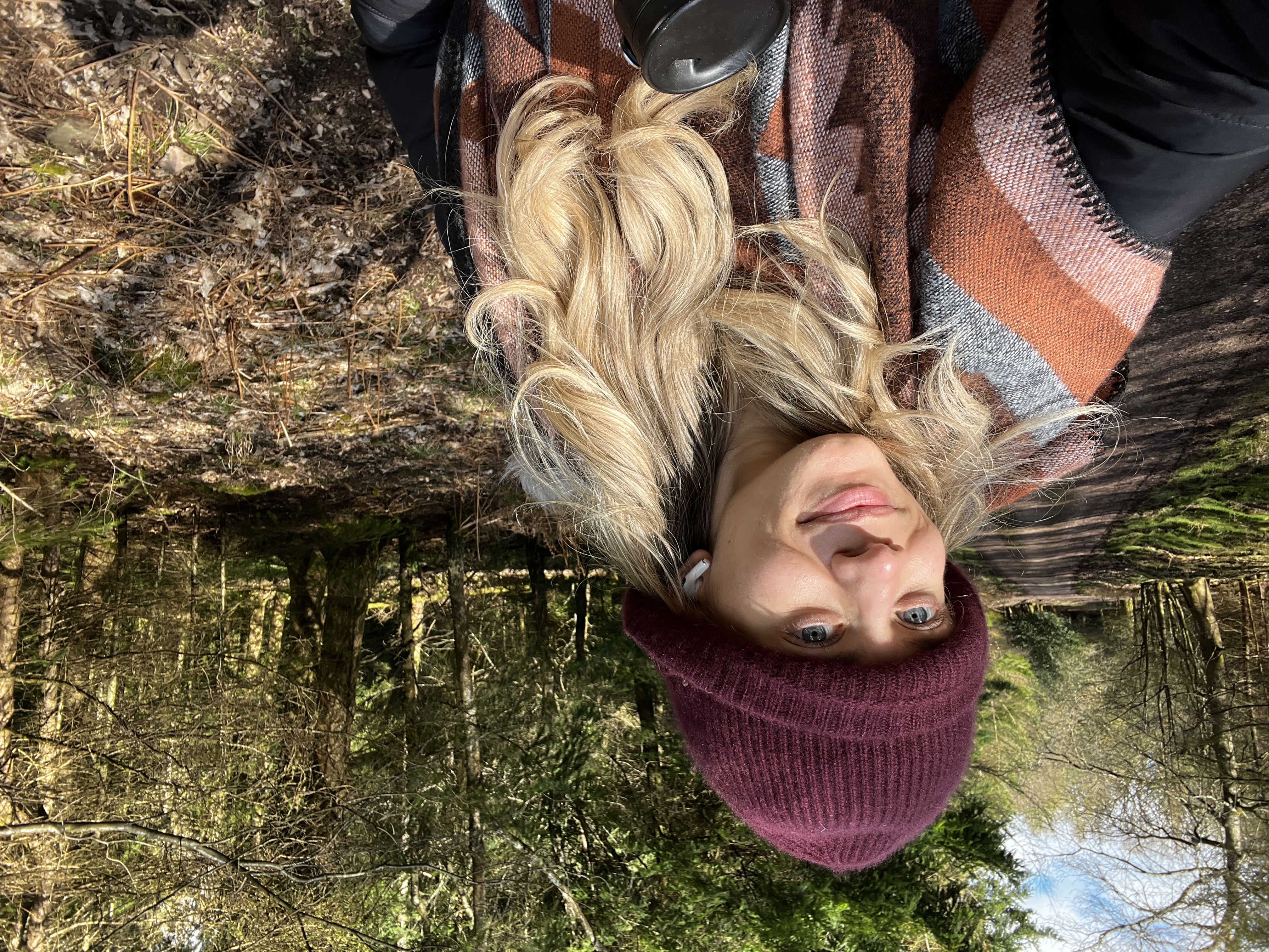 Sabrina Stocker standing in a forest, sunlight illuminating her face as she reflects on the beauty of nature during a cacao ceremony.