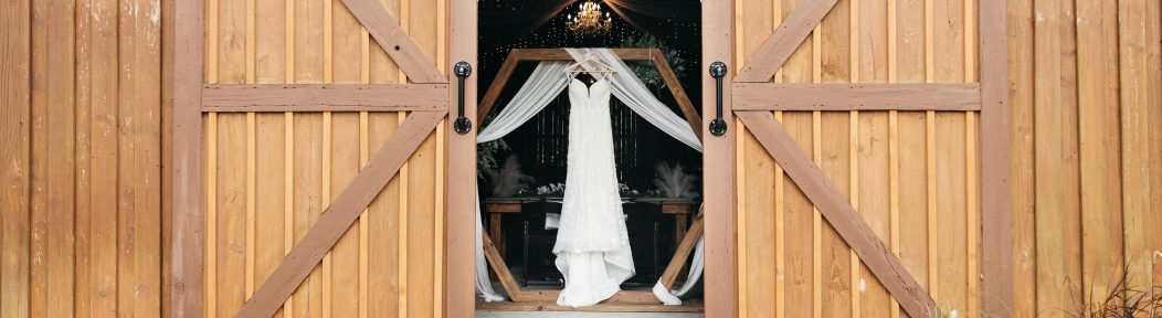 A wedding dress hanging in the open doorway of the barn