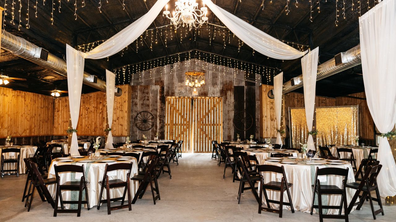 Reception tables set with white linens and black chairs inside the barn
