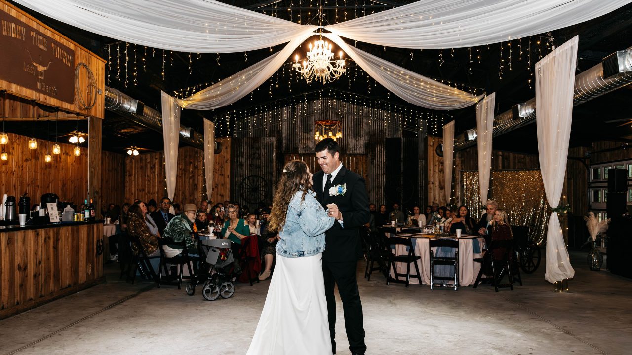 A couple sharing their first dance inside the draped, string-lit barn at Lazy P Ranch