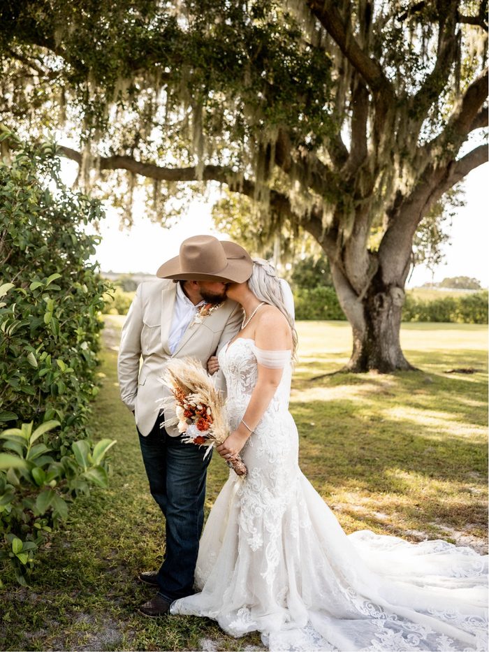 A couple in a cowboy hat and lace gown beneath the mossy oaks