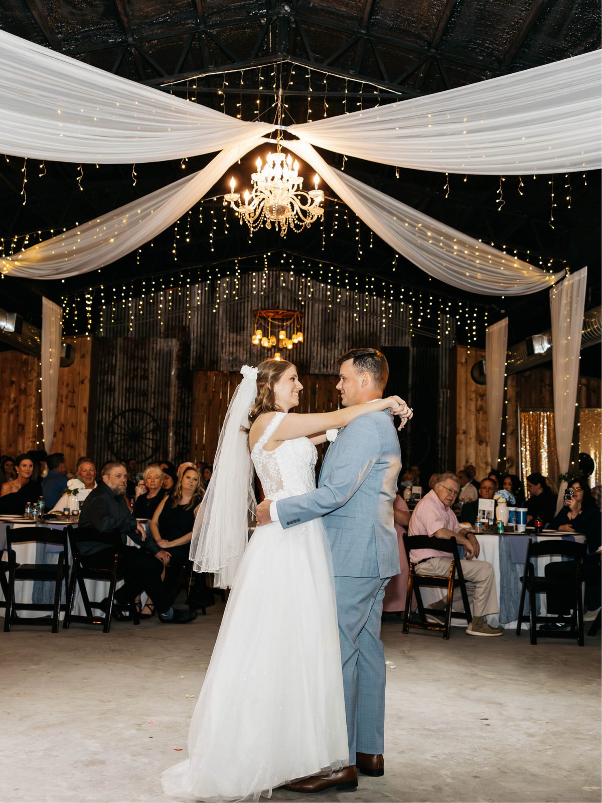 A couple dancing in the barn among candlelit tables and autumn florals