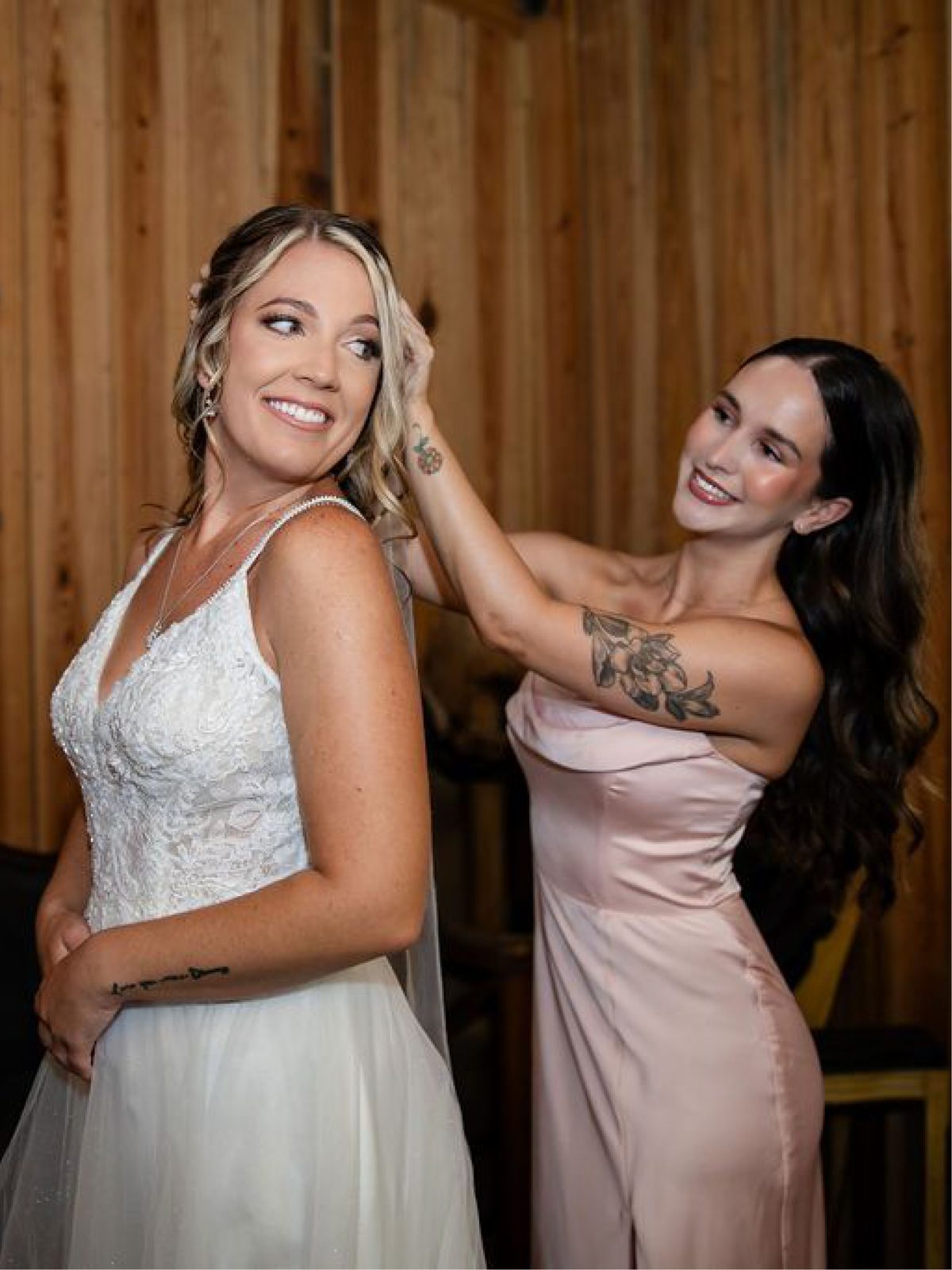 A bridesmaid fixing the bride's hair against the barn's wood wall