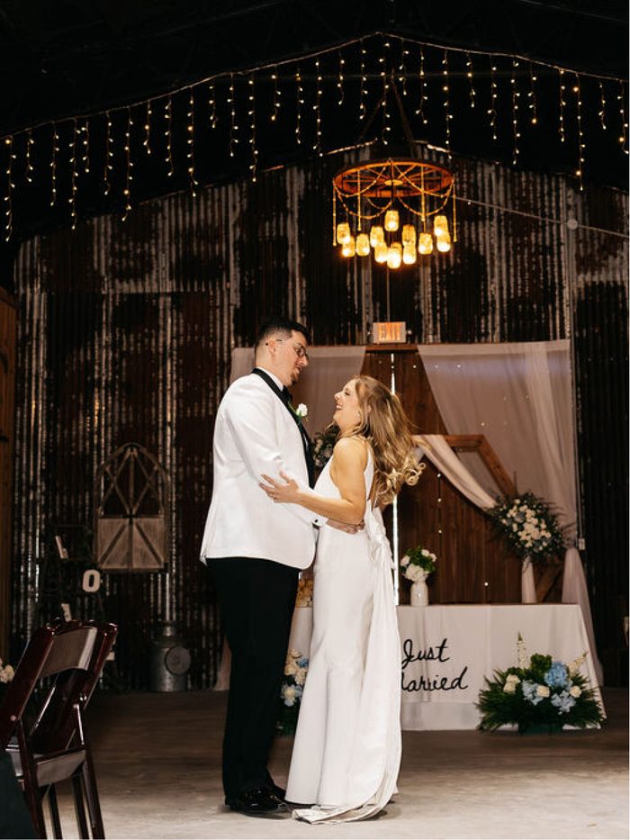 A couple dancing alone in the draped, string-lit barn
