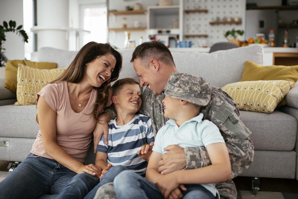 A military family laughing together on the couch at home