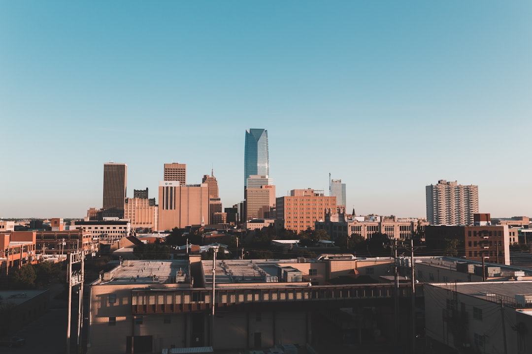 Oklahoma City downtown skyline at golden hour under a clear blue sky, low rooftops in the foreground.