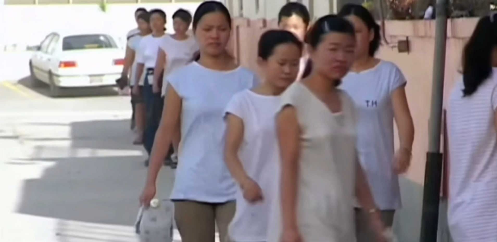 Contemporary documentary photograph of Asian garment workers exiting a factory in Saipan at dusk, neon signs and palm trees in the background, subdued color palette Contemporary documentary photograph of Asian garment workers exiting a factory in Saipan at dusk, neon signs and palm trees in the background, subdued color palette