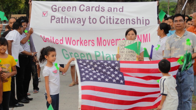 Archival-style photo of a peaceful street march on Saipan with people holding handmade signs about unity, workers' rights, and CNMI democracy, cloudy tropical sky overhead Archival-style photo of a peaceful street march on Saipan with people holding handmade signs about unity, workers' rights, and CNMI democracy, cloudy tropical sky overhead