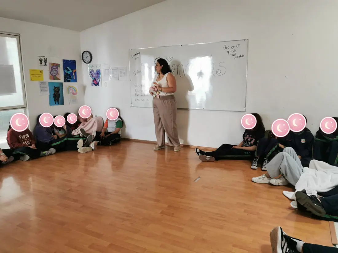 Marlene da una charla a un grupo de alumnas sentadas en el piso de un salón.