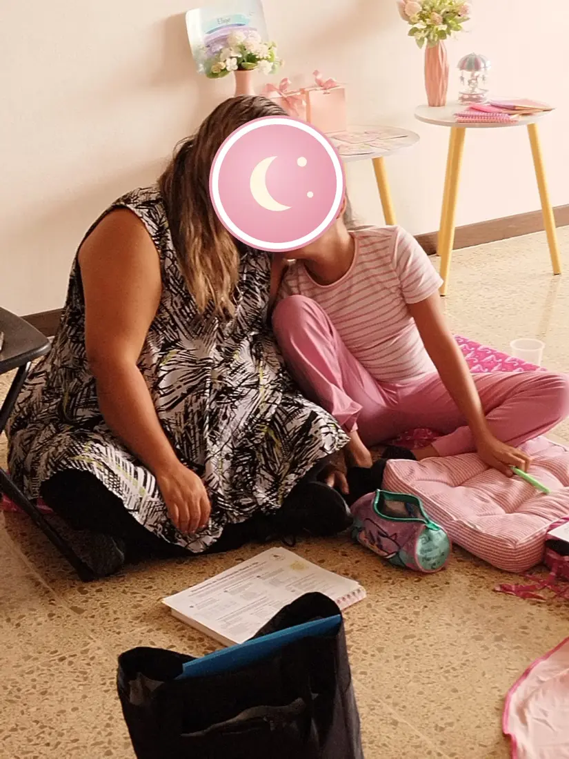 Una mamá y su hija sentadas juntas, recargadas una en la otra.