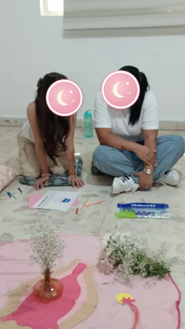 Una niña y su mamá trabajan sentadas en el piso con material del taller.