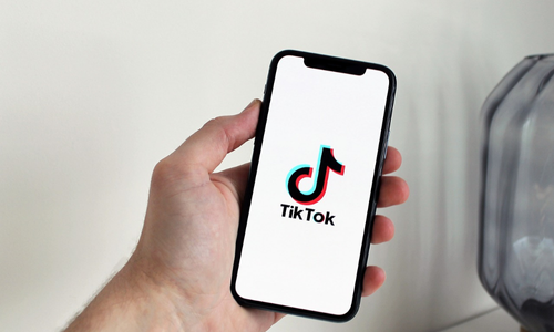 Close-up of a hand holding a smartphone with the TikTok logo on screen, symbolizing mobile social media marketing and video content engagement.