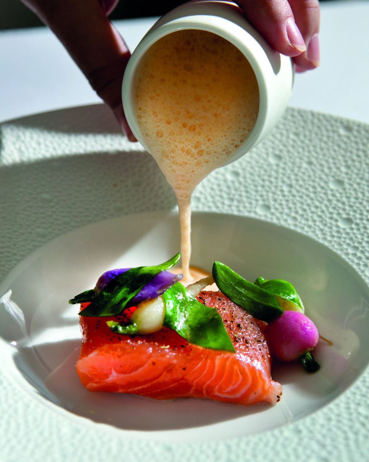 Een warme bouillon wordt uit een kannetje over een gerecht met zalm geschonken.