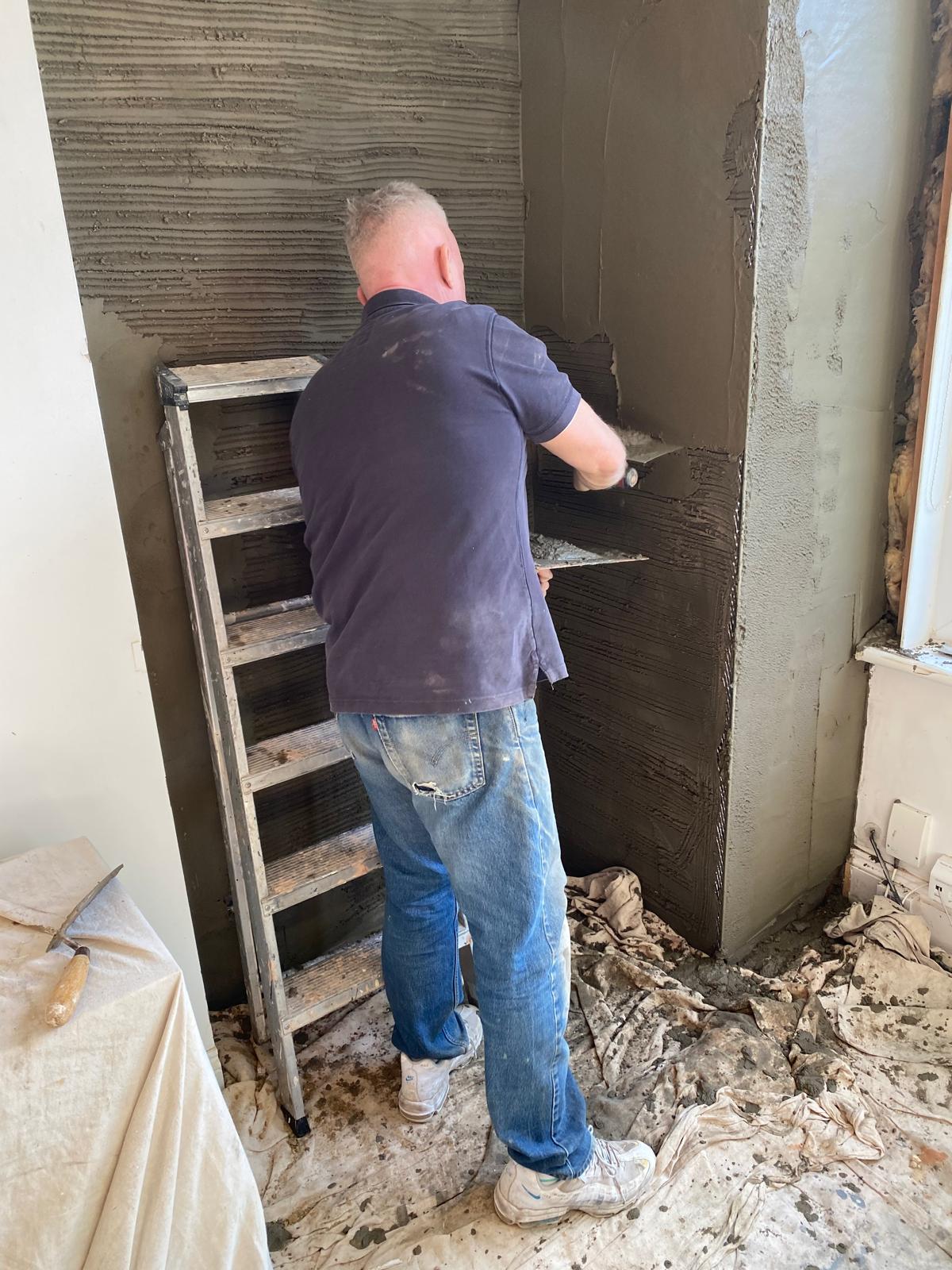 Plasterer applying render coat to internal corner during replastering preparation before decorating in Epsom