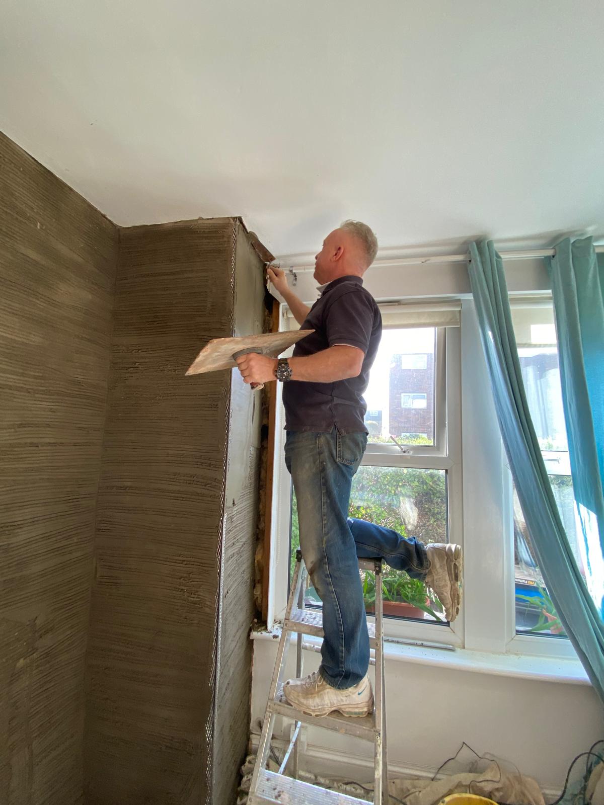 Jonathan Mills plasterer working on window reveal during internal wall plastering job in Epsom Surrey